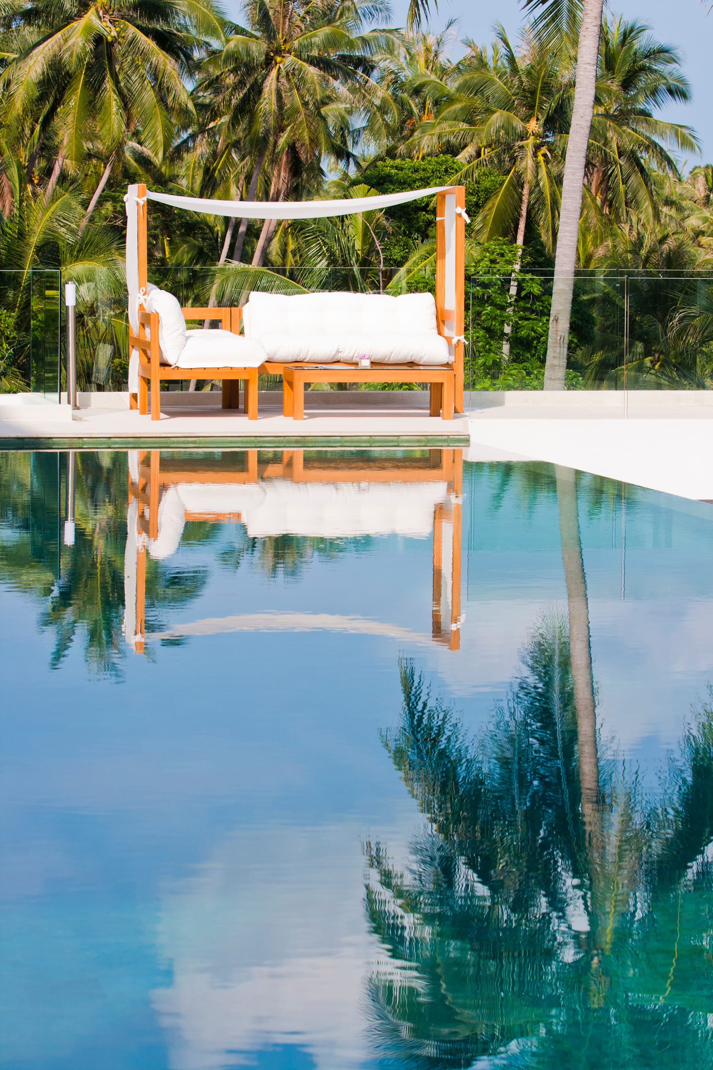 A teak daybed reflected in the still surface of the pool